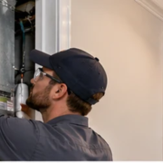 HVAC technician inspects an air handler and ductwork in a multilevel home, with an upstairs air register visible.