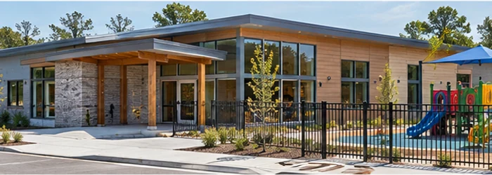 Single-level early learning center with an accessible entrance and fenced play yard, designed for a nursery facility.