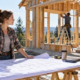 Homeowner acting as the general contractor reviews house plans with tradespeople at a timber-framed residential construction site.