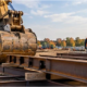 Excavator works beside heavy structural steel beams at a jobsite, illustrating robust construction equipment and materials.