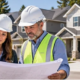 Homebuilding team reviews residential plans beside a development of completed houses.