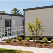 Portable modular classrooms line a school walkway with accessible ramps and the main school building nearby.