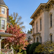 Queen Anne home with a turret stands beside an Italianate residence with tall windows and bracketed eaves, showing two Victorian styles.