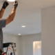 Electrician fits flush recessed ceiling lights and a built-in wall niche set back from the surface in a modern room.