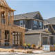 Builders frame houses in a new residential neighborhood, showing home construction activity in a growing community.