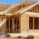 Builder checks the wood framing of a detached residential house under construction in a suburban setting.