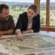 Residents and a planning professional review a residential development plan beside rural homes and farmland.