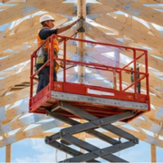 Worker on a raised scissor lift beneath vaulted timber scissor trusses in an unfinished building, illustrating two common construction uses of the term.