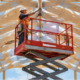 Worker on a raised scissor lift beneath vaulted timber scissor trusses in an unfinished building, illustrating two common construction uses of the term.