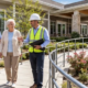 Accessible senior housing residence with a broad ramp, handrails, level courtyard paths, and an older couple reviewing the entrance with a construction professional.