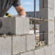 Mason lays one layer of concrete block, with the exposed wall edge showing the single-skin construction.