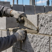 Mason lays rough-textured split-face concrete masonry block, showing the stone-like face and even mortar joints.