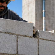 Mason aligns concrete blocks in stack bond, with each vertical joint directly above the next along a modern wall.