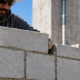 Mason aligns concrete blocks in stack bond, with each vertical joint directly above the next along a modern wall.