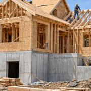 Residential home midway through construction, from the concrete foundation and timber framing to roof sheathing as builders install the roof structure.