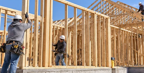 Carpenters assemble dimensional lumber studs and roof trusses on site for a traditional stick-built house.