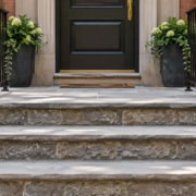 Raised masonry stoop at a townhouse entrance with a broad landing, three steps, and handrails on both sides.