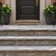 Raised masonry stoop at a townhouse entrance with a broad landing, three steps, and handrails on both sides.