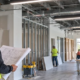 Commercial tenant improvement in progress as a contractor reviews plans while partitions, HVAC, and lighting are installed in a leased office.