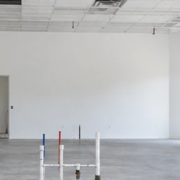 Empty commercial white-box suite with finished white walls, a basic ceiling grid, concrete floor, utility stubs, and a contractor inspecting it for tenant fit-out.