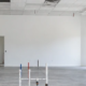 Empty commercial white-box suite with finished white walls, a basic ceiling grid, concrete floor, utility stubs, and a contractor inspecting it for tenant fit-out.